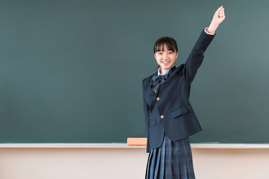 Female elementary, middle, and high school students in blazers stand in front of the blackboard and strike a triumphant pose.