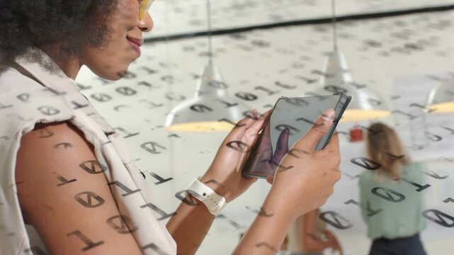 Woman tapping tablet in open office activating binary overlay and analyzing tech data while smiling