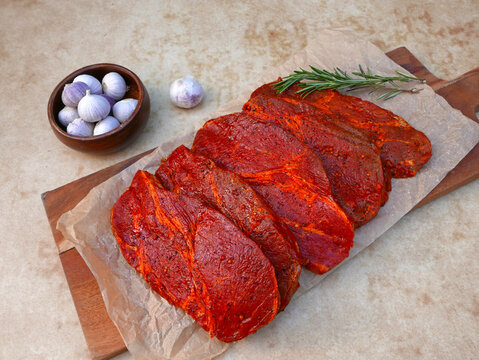 Marinierte Schweinenackensteaks mit Knoblauch und Rosmarin auf rustikalem Holzbrett.