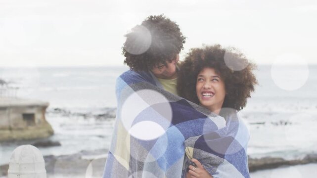 Man draping blanket around woman, leaning and nuzzling while bokeh fading, giving warmth for travel