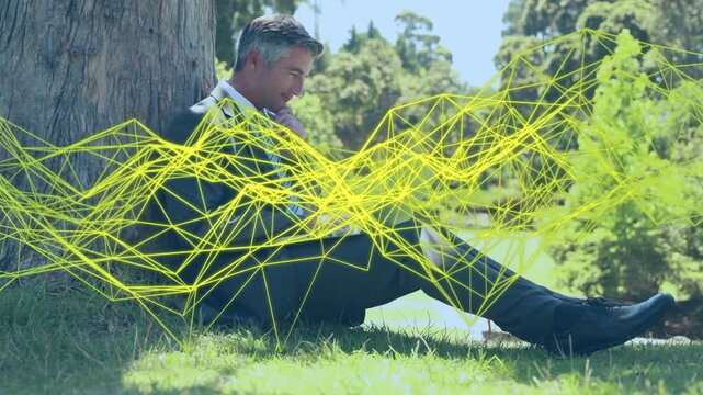 Mature man typing on laptop under tree, activating yellow wireframe and analyzing business data