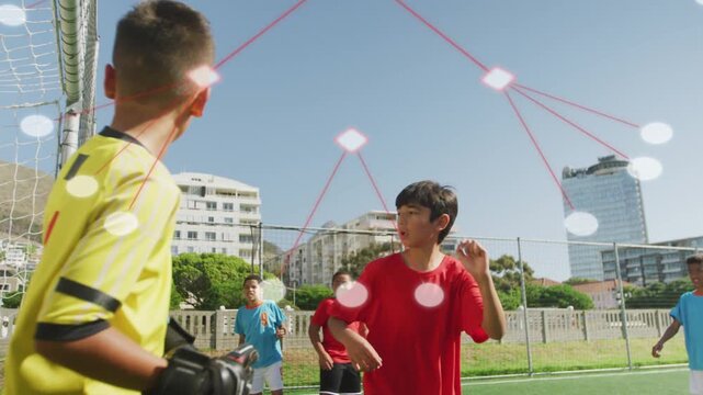 Group of boys tracking incoming ball, defending goal on sports pitch, AR overlay mapping trajectory