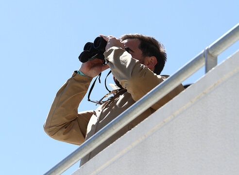 Hombre usando prism&aacute;ticos binoculares observando y vigilando atento con gemelos con lente largavistas desde arriba