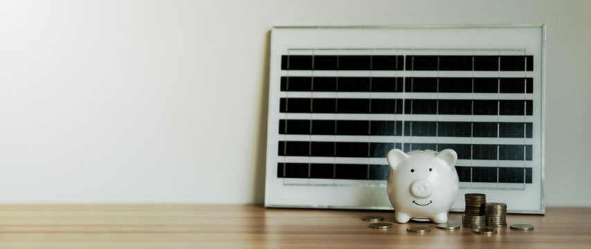 White piggy bank sits beside solar panel. Coins rest nearby, symbolizing savings. Clean background highlights eco-friendly lifestyle. Solar panel emits energy for sustainable living