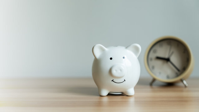 White piggy bank smiles gently on wooden surface. Round clock ticks softly in background. Simple scene suggests saving and time. Ideal for finance, budgeting, or planning concepts