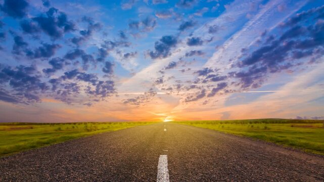 asphalt road among a green prairie at the sunset time lapse scene