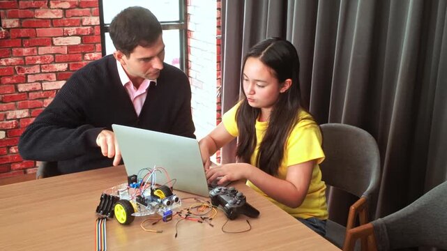 Mentor guides a student building a wheeled robot, programming with a laptop amid wires and sensors during a hands-on STEM electronics session