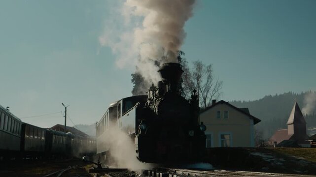 Steam train Mocanita waits at the station in Romania. Clouds of steam rise as the locomotive prepares for the next journey. A classic experience for train lovers.