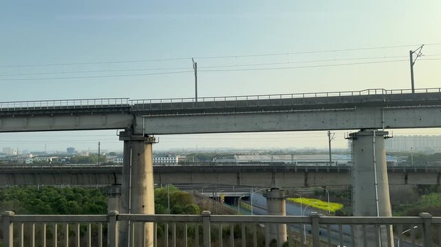 Elevated high-speed railway viaduct in Suzhou, China during spring. Multiple concrete bridge levels with catenary wires cross over a highway tunnel entrance.