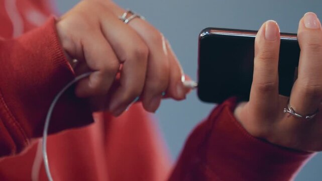 Closeup hands plugging earbuds into smartphone, white female in red hoodie, silver rings on fingers, slow deliberate motions, intimate listening ritual, soft cinematic lighting, shallow depth
