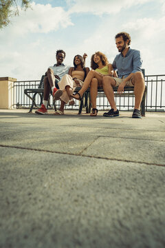 Group of friends sitting together on bench enjoying summer day