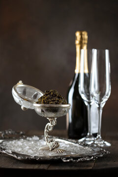 Black caviar and champagne. Exquisite serving of black caviar. Glasses and bottle of champagne are out of focus. Black caviar is served in dish with ice. Concept for holiday