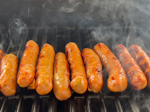 Sausages turning golden brown with visible smoke