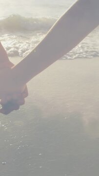 Vertical video: Couple walking shore, romance, other hand reaching, joining hands, waves lapping