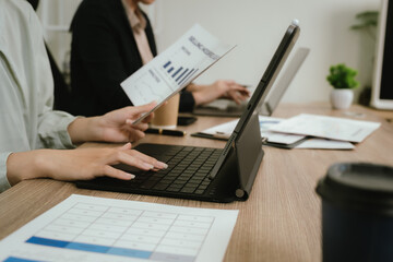 Fototapeta premium Close-up of business professionals reviewing financial reports and charts on a desk, pointing at data with documents, laptop, and smartphone in a modern office.