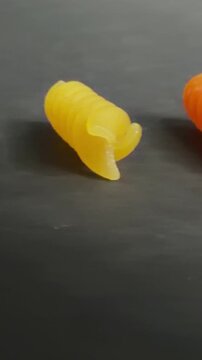 Colorful uncooked snail shaped fusilli pasta rotating slowly on a dark, textured background, revealing intricate details of the semolina and vegetable powder ingredients