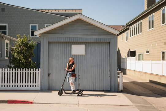 Woman on electric scooter by a garage on sunny California street
