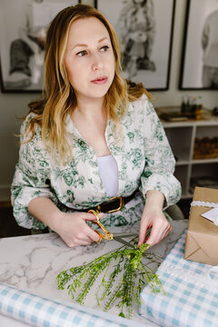 Woman wrapping gift with greenery at home