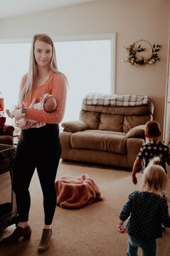 Young mom holding newborn with two small children walking by