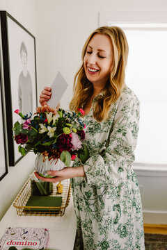 Smiling middle aged woman holding flowers and reading note