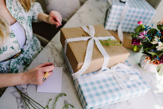 Woman writing card beside wrapped gifts
