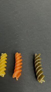 Colorful uncooked tricolor fusilli pasta with tomato and spinach flavor spinning and dancing on a dark stone background, showcasing a healthy and vibrant meal ingredient