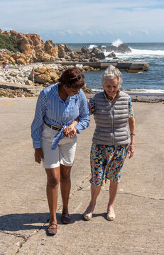 Western Cape South Africa. 05.11.2026. .Two women of different ages and ethnicities share a moment of connection while walking together on a sunny day by the sea, with crashing waves in the background