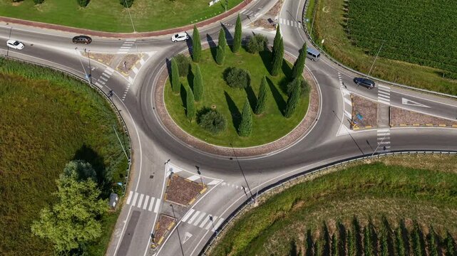 Wide angle 4K drone shot of a busy traffic circle in Italy, capturing the contrast between asphalt pavement infrastructure and the natural beauty of the vineyards.