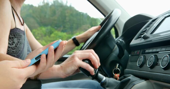 A woman&rsquo;s hands are at the wheel, and the co-driver&rsquo;s hands, holding a phone in the foreground, are guiding the way