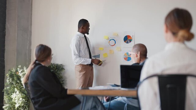 Business conference, african man presenting financial report for colleagues. Teamwork in international company, coworkers listening to presentation of startup owner, investments and economic risks