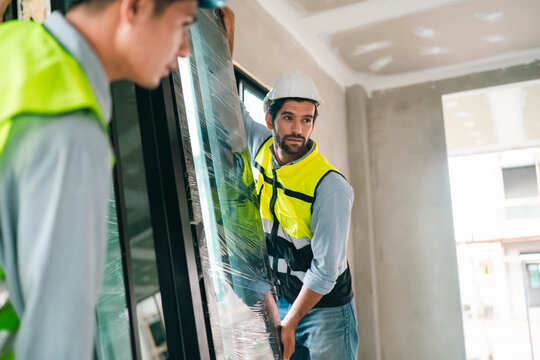 Construction worker safety helmet protective vest window installation indoor renovation glass panel apartment interior laborer building site manual handling
