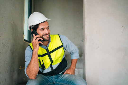 Construction worker with hard hat using mobile phone, smiling in interior site