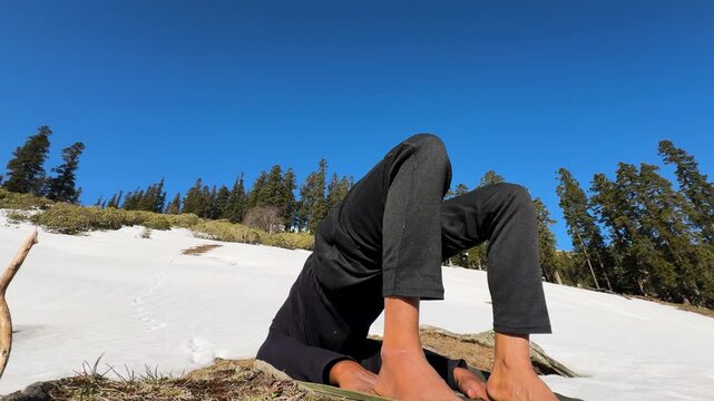 person practicing yoga headstand on snowy mountain landscape with pine trees and clear blue sky
