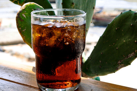 Cola drink with ice cube and beach