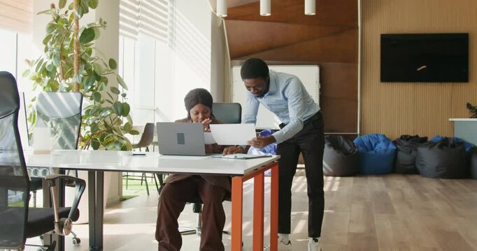 Black manager reviewing paperwork with black colleague at desk