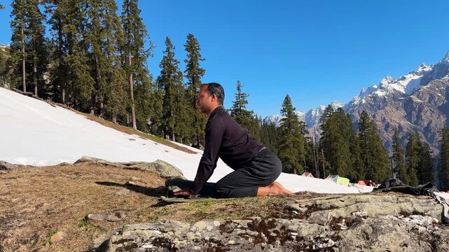 person practicing yoga headstand on mountain slope with snow patches and pine forest under blue sky