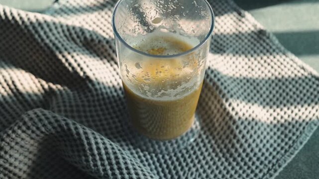 A glass filled with a cool drink sits on a patterned fabric, showcasing light and shadow effects.