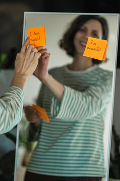 Smiling reflection placing self love affirmation on mirror