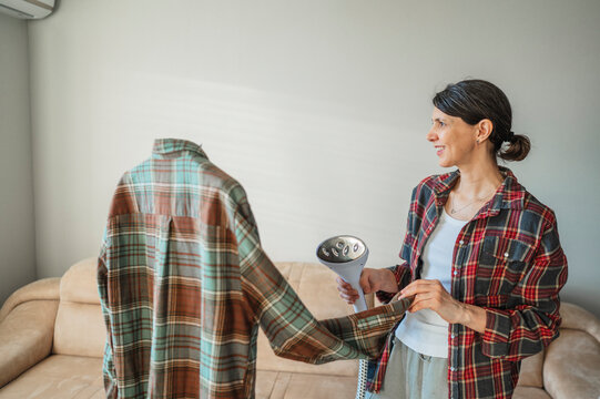 Woman ironing plaid shirt with steam iron in living room