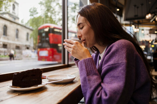 Woman enjoying coffee and cake in a London cafe by the window