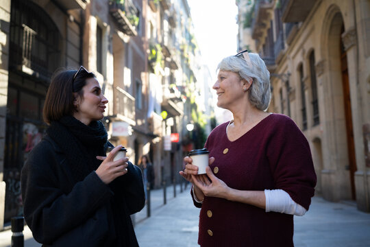 Two women enjoying coffee and conversation on a bustling city street during the daytime