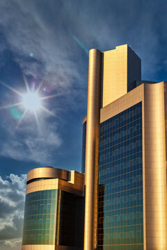 Modern Golden Skyscraper with Glass Facade Under a Bright Sun and Blue Sky