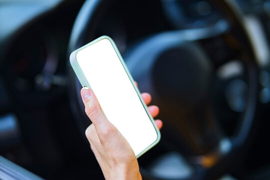 Hand holding a smartphone with a blank screen inside a car