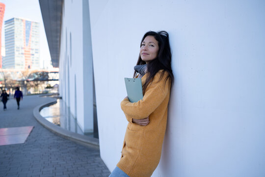 Confident professional holding folder leaning against city wall