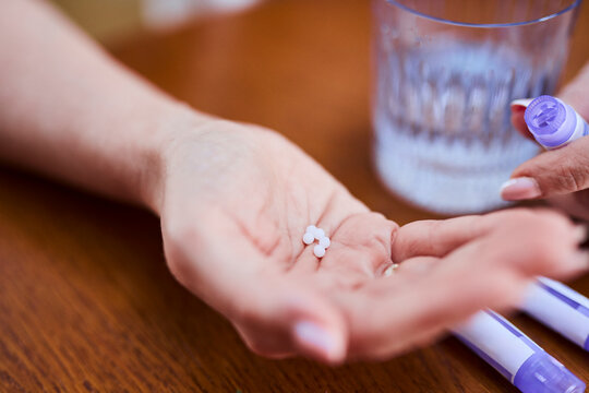 Hand holding pills and homeopathic medicine with glass of water