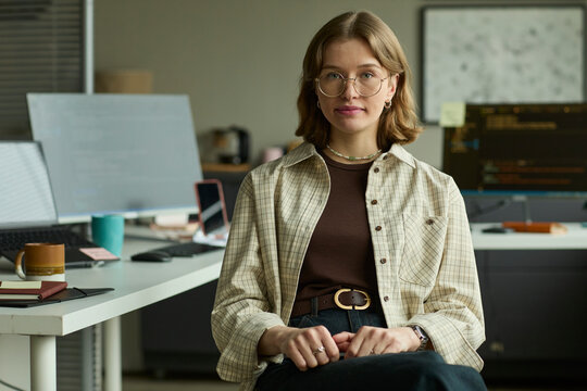 Manager sitting at desk in modern office looking at camera