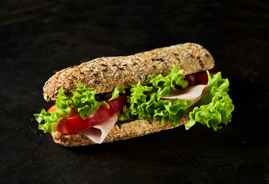 Fresh organic turkey baguette sandwich with tomato on dark background