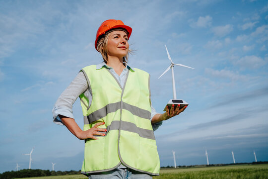 Engineer with hand on hip holding model of wind turbine at field