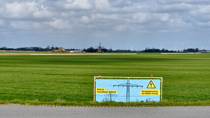 Obraz premium Protest Against High Voltage Power Lines In Rural Obdam Netherlands With Warning Sign And Windmills In Green Fields Energy infrastructure and rural development concerns showing a warning sign