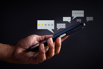 A hand holds a smartphone displaying low star rating bubbles on a dark background. Negative...